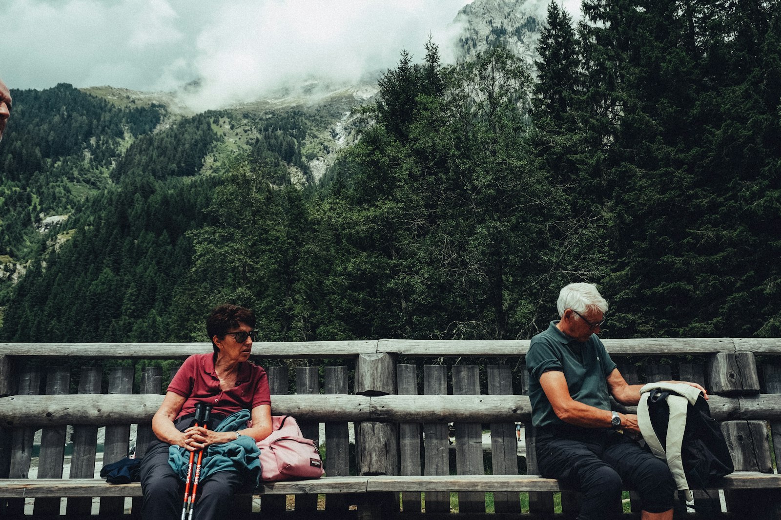 Dos personas descansan en un banco con las montañas de fondo